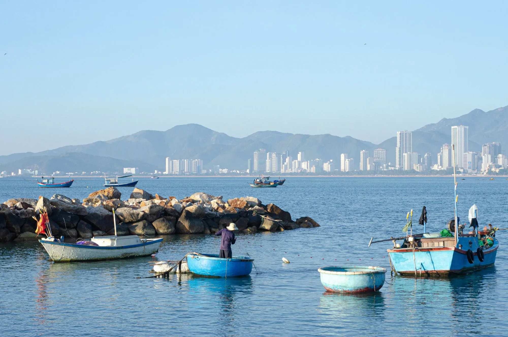Thuyền thúng và thuyền đánh cá trên vịnh Nha Trang, phía xa là thành phố và núi.